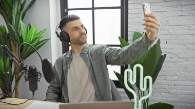 Genç bir İspanyol, modern radyo stüdyosunda akıllı telefonuyla selfie çekiyor..
