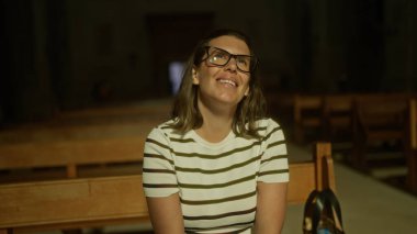 İtalya 'da bir kilisede oturan, gülümseyen ve gözlüklü, çizgili tişörtlü güzel bir İspanyol kadın..