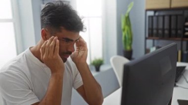 Ofiste çalışan ve stresli hisseden bir adam. Pencere kenarında bilgisayar ve bitkiler olan.