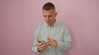 Akıllı telefonu elinde tutan genç adam pembe arka plana karşı endişeli bir ifade takınıyor.