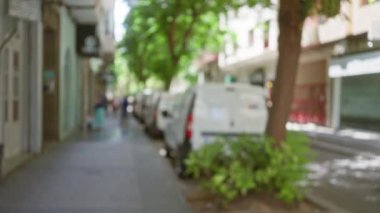 Bulanık insanların yürüdüğü, park halindeki arabaların ve yeşil ağaçların açık hava şehrinde yumuşak bir bokeh etkisi yarattığı bir şehir caddesi..