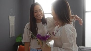 Anne ve kızı birlikte oturma odasında, gülümsüyor ve kucaklıyor. Çiçekleri sıcacık bir evde tutuyorlar.