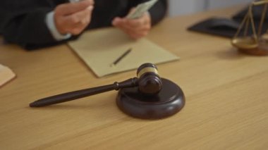 Yargıç, ahşap bir masada, içi tokmak ve teraziyle para sayıyor.