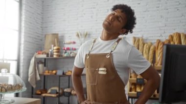 Fırında çalışan genç adam, kapalı dükkânda fırınların ve hamur işlerinin arasında dikilirken boynunu uzatıyor.