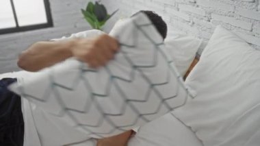 Yakışıklı genç adam rahat bir yatak odasında beyaz yastıklar ve tuğla duvarlarla uzanıyor, rahat görünüyor ama uyuyamıyor..