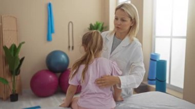 Kadın fizyoterapist ve genç kız klinik odasında modern ve iyi donanımlı bir çalışma alanındaki terapi seansında tedavi planını tartışıyorlar.