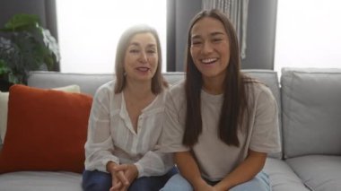 Evdeki bir kanepede birlikte oturan kadınlar mutlu ve rahat görünüyor, sıcak bir oturma odasında sevgi dolu bir anne-kız ilişkisini tasvir ediyorlar..