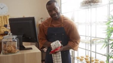 Gülümseyen adam sıcak fırında yemek kurutuyor taze hamur işleri ve kurabiyeler sergileniyor, parlak iç mekan ve neşeli atmosferle çevrili..