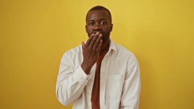 Afro-Amerikalı adam ayakta duruyor, elini havaya kaldırarak öpüşüyor, izole edilmiş sarı arka planda sevimli yüz ifadesi seksi ve kendinden emin cazibeyi yakalıyor.