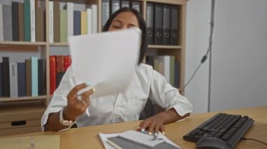 Ofiste masa başında çalışan, dosya ve dosyalarla çevrili, iş yeri aktivitelerini ve kadın profesyonel çabalarını sergileyen bir kadın.