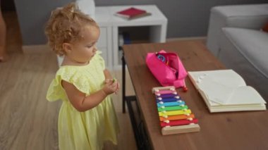 Oturma odasında renkli ksilofon ve pastel boyalarla oynayan küçük bir kız.