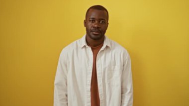 Afrika kökenli Amerikalı bir adam ayakta duruyor ve el yazısı yapıyor. İzole edilmiş sarı arka planda başarı ve olumlu bir ifade sergiliyor.