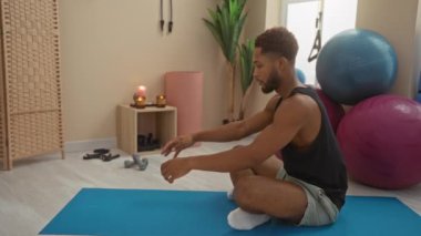 Spor salonunda mavi hasırda uzanan adam spor topları, bitkiler, mumlar ve dingin ve odaklanmış bir spor ortamını gösteren ekipmanlarla çevrili.