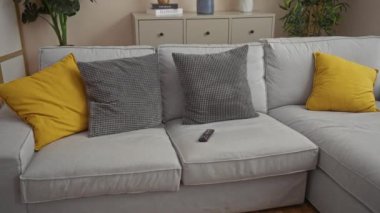 Orta yaşlı bir çift, rahat bir oturma odasında gri bir koltukta oturup uzaktan kumandayı elinde tutan adamla eğlenirken kadın arka planda sarı yastıklarla gülümsüyor ve rahatlıyor.