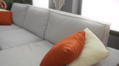 Evdeki video görüşmesi sırasında koltukta oturan genç İspanyol adam elinde telefonla modern apartman dairesinde mutlu bir şekilde iletişim kuruyor.