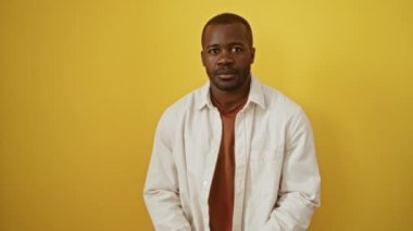 Endişeli Afro-Amerikalı bir adam tişört giyiyor elleri tedirgin, izole edilmiş sarı arka planda çivi yiyor, stres ve anksiyete sorunu var.