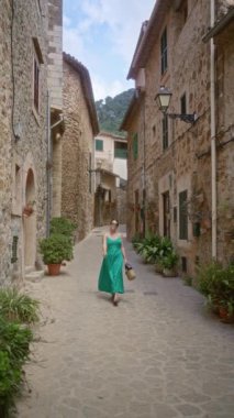 Yeşil elbiseli kadın Valldemossa, Mallorca, İspanya 'da dar bir taş sokakta yürüyor güneşli bir günde geleneksel mimari ve Akdeniz cazibesini sergiliyor..