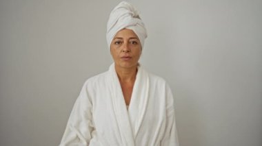 Bornoz ve havlu giymiş bir kadın, gülümseyen yüzüyle gözlerini kapatıyor, şaşırarak gözlerini çeviriyor - beyaz, soyutlanmış, orta yaşlı, İspanyol bir kadın.
