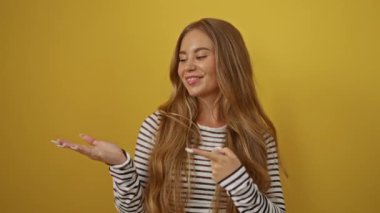 Sarı çizgili tişört giyen genç sarışın kadın, elini gösteriyor, şaşırmış ve gülümsüyor.