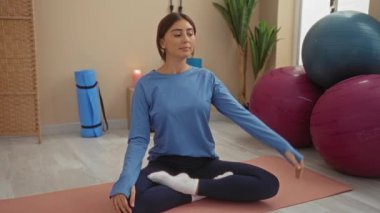 Spor kıyafetleri giymiş spor topları ve minderlerle spor salonunda yoga yapan genç bir kadın..