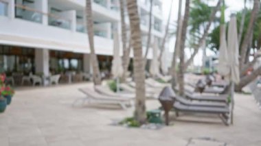 Bulanık palmiye ağaçları ve lüks bir ortamda şezlongların bulunduğu tropik bir tatil köyünün odaksız manzarası.