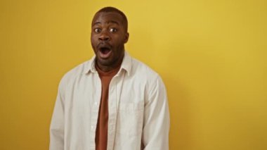 Afroamerikan gömlekli adam şişirilmiş yanakları ve komik yüz ifadesiyle, izole edilmiş sarı arka planda çılgın ağızlı.