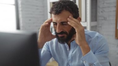 Modern ofis ortamında bilgisayarla çalışan sakallı stresli bir adam.