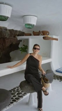 Jameos del agua, Lanzarote 'da volkanik taş koltukta oturan siyah elbiseli bir kadın. Etrafı beyaz duvarlar ve eşsiz dekorlarla çevrili.