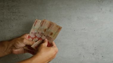 Kolombiya pezolarını sayan bir adam, somut bir arkaplan karşısında, yerel para birimini vurguluyor..