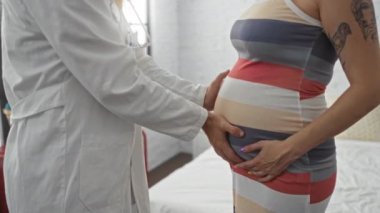 Doktor yatak odasında hamile kadının karnını muayene ediyor.