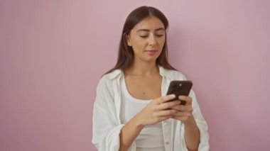 İzole edilmiş pembe arka plan üzerinde akıllı telefon kullanan genç bir kadın. Yüzünde neşe ve şaşkınlık gibi ifadeler var.