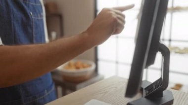 Fırında dokunmatik ekran kullanan genç bir adam. Kapalı mekanda kot önlük giyiyor ve ekranı işaret eden eline odaklanıyor.