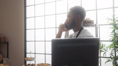Fırında çalışan genç adam telefonda konuşuyor. Etrafı pastalar ve pastalarla çevrili..