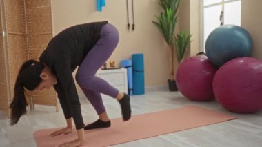 Spor salonunda pilates toplarıyla egzersiz yapan, paspasın üstünde yoga yapan, dingin fitness merkezinde esnek pozlar veren bir kadın..