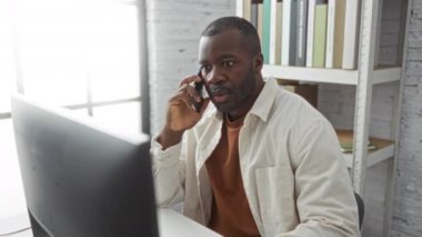 Modern ofis ortamında telefonla konuşan yakışıklı bir adam. Arkaplanda kitaplıklar var.