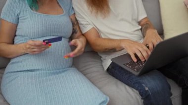 Kredi kartı olan hamile bir kadın ve dizüstü bilgisayarı olan bir adam kapalı koltukta oturuyor.