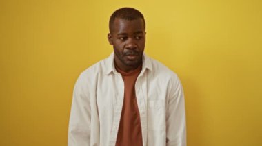 Afro-Amerikalı bir adam tişörtünü giymiş, şaşırmış bir ifadeyle dikiliyor ve izole edilmiş sarı arka planda ağzını açıyor.