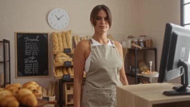 Fırının içinde gülümseyen bir kadın tezgahın arkasında duruyor. Etrafında ekmek ve hamur işleri var.