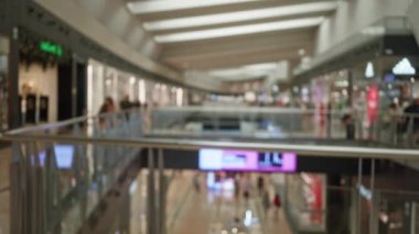 Alışveriş merkezinin içi bulanık. Mağazada gezinen, arka planda modern bir çatı altında bokeh ve odaklanmış ışıkları gösteren odaksız müşterilerle dolu..
