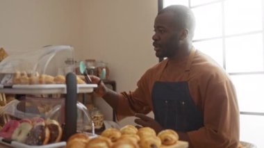 Pastanedeki genç adam elinde mavi bir önlükle elinde maşayla hamur işlerine uzanıyor.