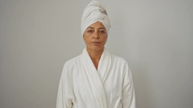 Havlu ve bornozlu kadın, izole edilmiş beyaz arka plan üzerinde ciddi bir parmak işareti yapıyor, sakin bir yüz ifadesiyle el hareketi yapıyor.