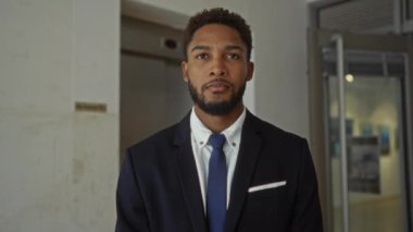 Young man in a suit standing indoors with arms crossed in an office setting