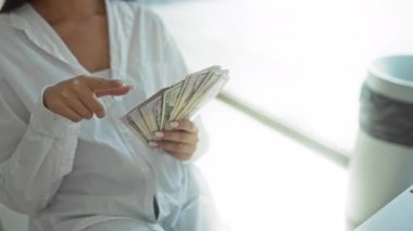 Dolar sayan bir kadın modern ofiste ellerini beyaz gömlek giyerek uzatıyor.