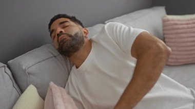Yumuşak yastıklı, rahat oturma odasındaki gri kanepede uyuyan İspanyol genç adam.