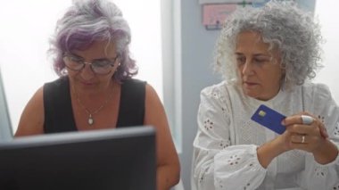 Bir ofiste çalışan iş kadınlarının birinde kredi kartı diğerinde ise dizüstü bilgisayar olması profesyonel ve işbirlikçi bir çalışma ortamı olduğunu gösteriyor.