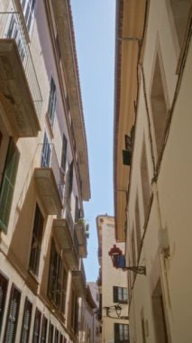 Palma 'daki geleneksel binalar, balkonlu mallorka ve açık mavi gökyüzünün altındaki sokak lambaları arasında mimari güzelliği vurgulayan dar bir ara sokak.