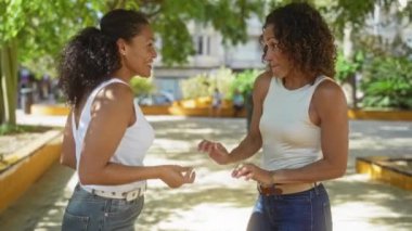 Şehir parkında ağaçlarla mutlu bir şekilde dans eden kadınlar, beyaz bluzlar ve kotlar giyerek, şehrin açık hava ortamında, neşeli bir etkileşim ve arkadaşlık göstererek yakalandılar.