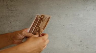 Beton bir arka planda Mısır sterlini tutan adam, bu para biriminin çeşitli değerlerini yakın çekimde gösteriyor, elleri ve parmakları renklendiriyor..