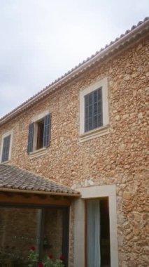 Geleneksel taş ev, mavi kepenkleri ve kırsal alanda seramik çatısı olan bulutlu gökyüzünün altında.