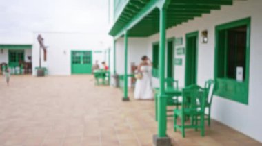 Bulanık yeşil sandalyeler ve masalar Lanzarote 'de bir terasa kurulmuş. Arka planda ve İspanyol mimarisinde insanlar var.